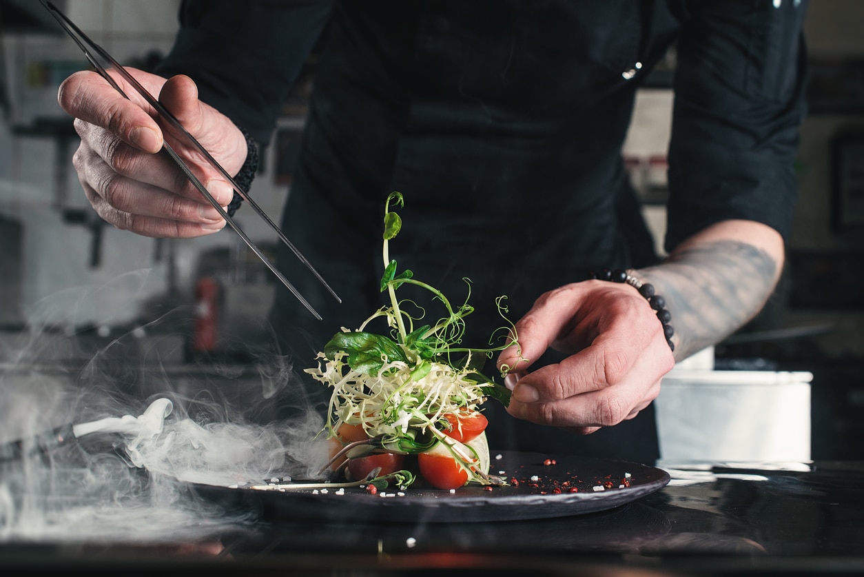 Chef finishing healthy salad on a black plate with tweezers. almost ready to serve it on a table